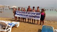  חברי אגודת הפסוריאזיס בישראל, מחזיקים שלט עם הכיתוב בעברית ובאנגלית על רקע ים המלח. צילום: אגודת הפסוריאזיס הישראלית.